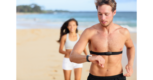 man running on beach checking heart rate watch wearing a monitor