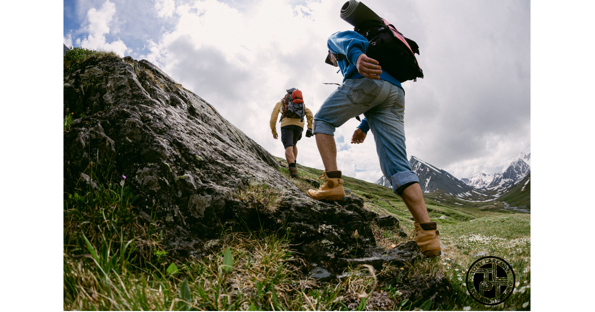 Two people hiking uphill with backpacks toward snow-capped mountains