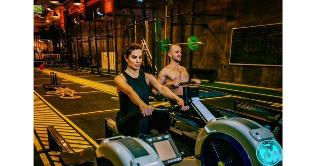 Man and woman performing indoor rowing workout in gym for fat loss and conditioning