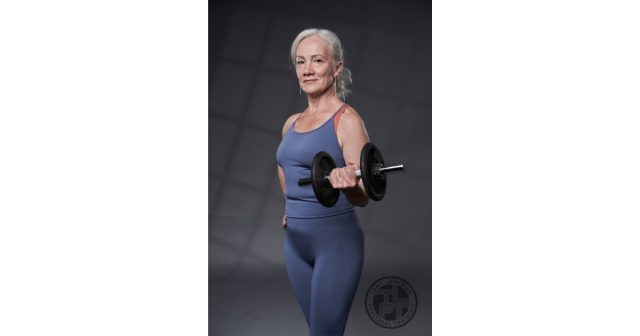 Woman over 50 performing a dumbbell curl to build muscle and maintain strength as she ages.
