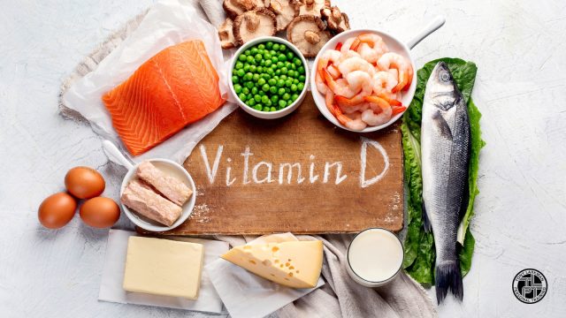 Selection of foods associated with vitamin D including salmon, oily fish, eggs and mushrooms, arranged around a wooden board labelled Vitamin D.