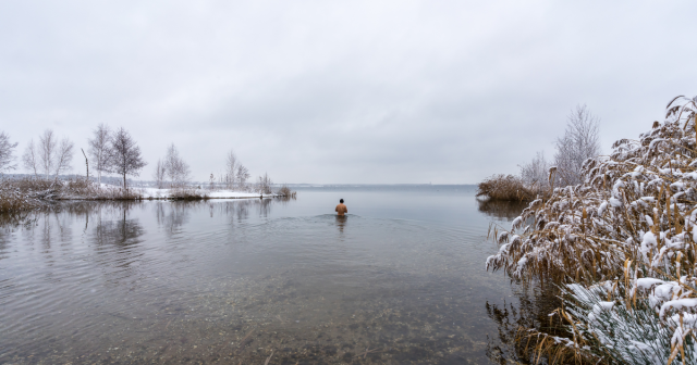 man wading out to swim in icy lake