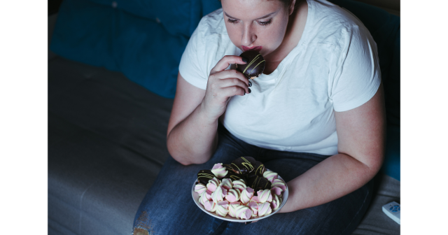 overweight woman eating biscuits on sofa watching tv