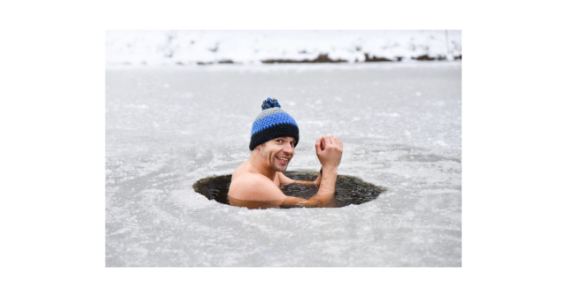 man with woolly hat submerged in a ice fishing hole